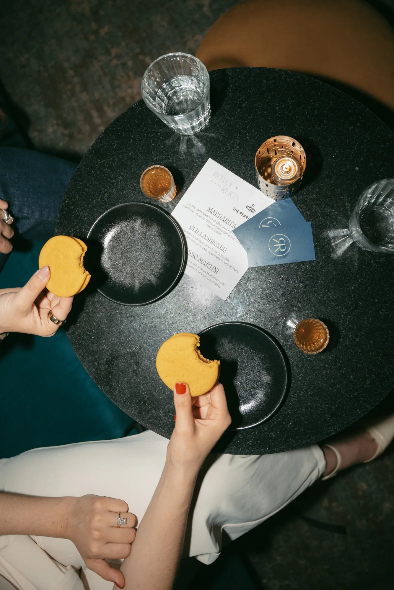 Two women at an event holding Royce + Reign Old Fashioned Cocktail-inspired cookies, the perfect premium event favor.