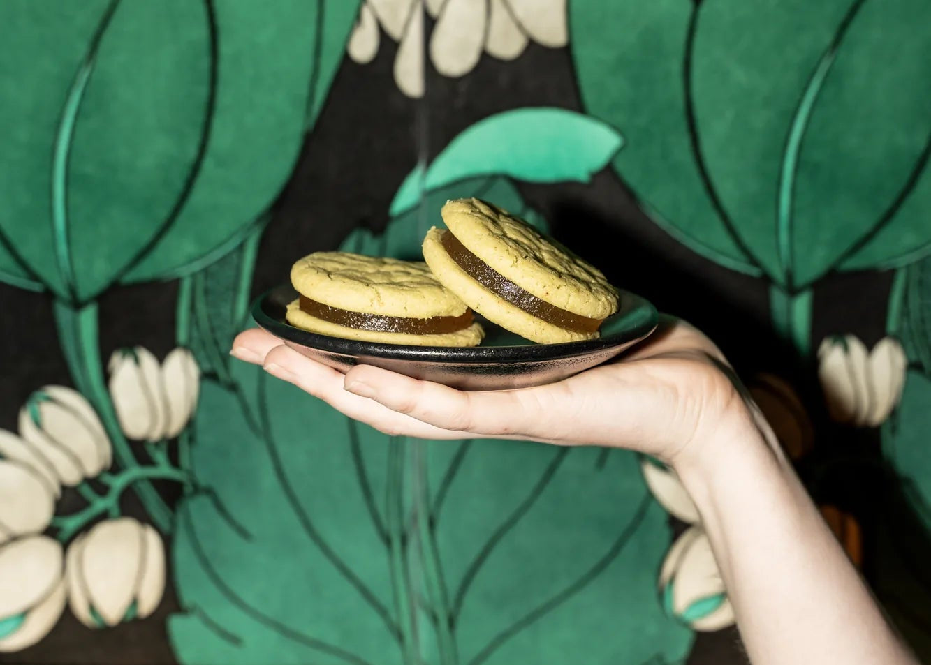 Hand holding a plate with Royce + reign Margarita cookies against a floral patterned background